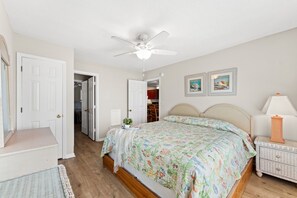 A bedroom with a bed, a nightstand, a lamp, a ceiling fan, and two framed pictures on the wall.