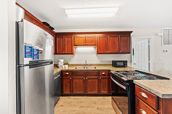 A kitchen with wooden cabinets, a stainless steel refrigerator, a microwave, and a stove. - Cassie - Pet Friendly, Oceanfront home in Cherry Grove (North Myrtle Beach)