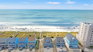 A coastal view with a beach, a boardwalk, and a row of houses with a view of the ocean.