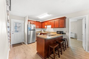 A kitchen with wooden cabinets, a stainless steel refrigerator, a built-in microwave, and a wooden island with stools.