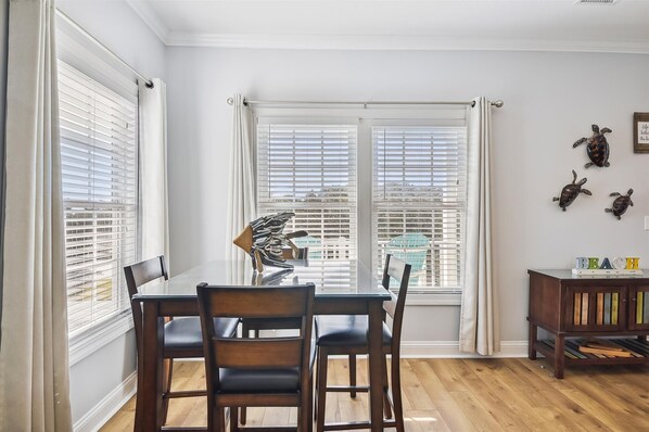 A dining area with a table and chairs, large windows with blinds, and a wall with turtle decorations.