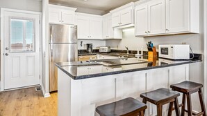 A modern kitchen with white cabinets, stainless steel appliances, a granite countertop, and a built-in island with bar stools. - Chase - Pet Friendly Oceanfront House in Cherry Grove (North Myrtle Beach)
