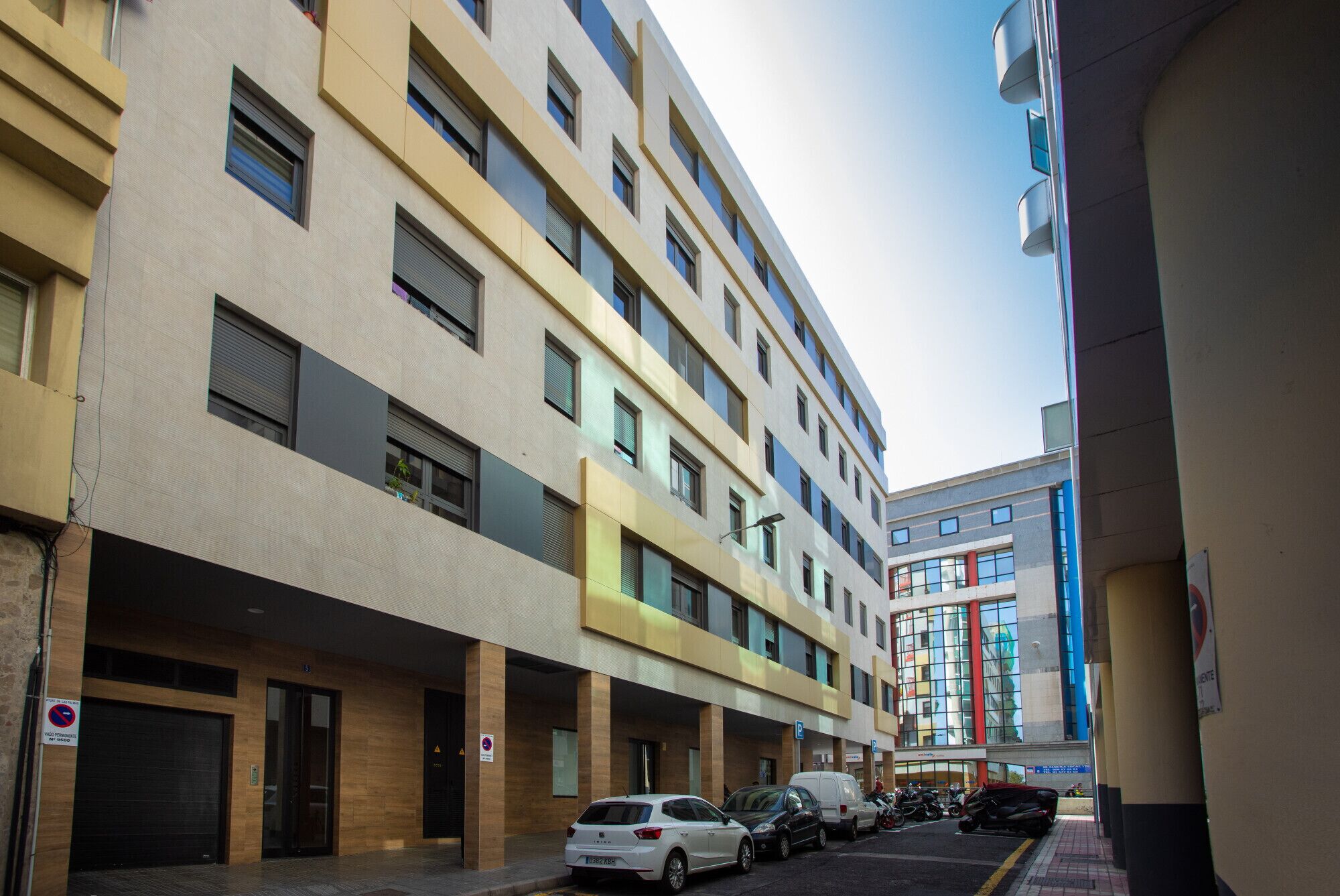 Un hotel de varios pisos con un diseño moderno, que cuenta con un patio central con coches y motocicletas estacionados.