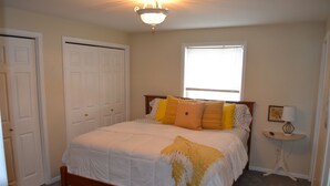 Un dormitorio con cama, una mesita de noche con lámpara, una ventana y una puerta.