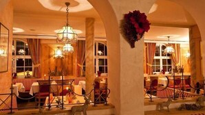 A warmly lit dining area with arched ceilings, chandeliers, and a central floral arrangement. - Tauernkoenig (Tweng)