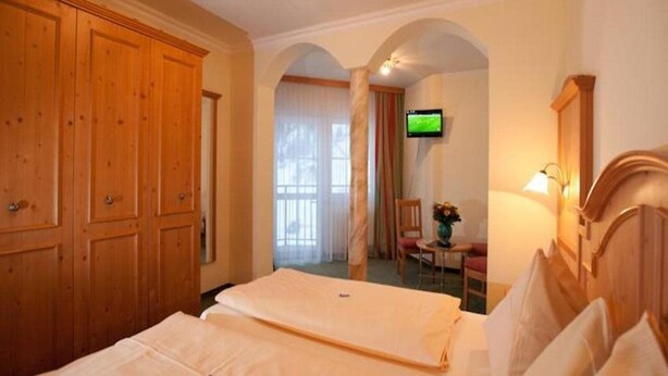 A hotel room with a bed, wooden wardrobe, TV, and a small table with a chair. - Tauernkoenig (Tweng)