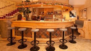 A bar area with a curved counter, multiple stools, and a variety of bottles and glasses on shelves. - Tauernkoenig (Tweng)