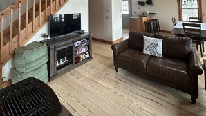 A spacious living room with a wooden staircase, a leather sofa, and a television.