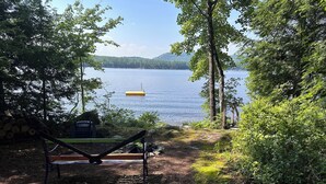 A lakeside view with a hammock, a colorful inflatable mattress, and a dock extending into the water.