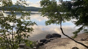 A wooden deck leading to a sandy beach with a calm lake and trees in the background.