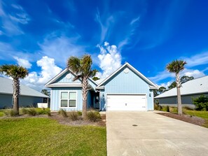 A light blue two-story house with a garage, surrounded by well-maintained lawns and palm trees.