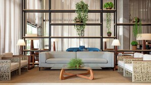 A modern living room with a sofa, coffee table, and wicker chairs. There are shelves with plants and a large window with curtains. - Hilton Garden Inn Itajai (Itajai)