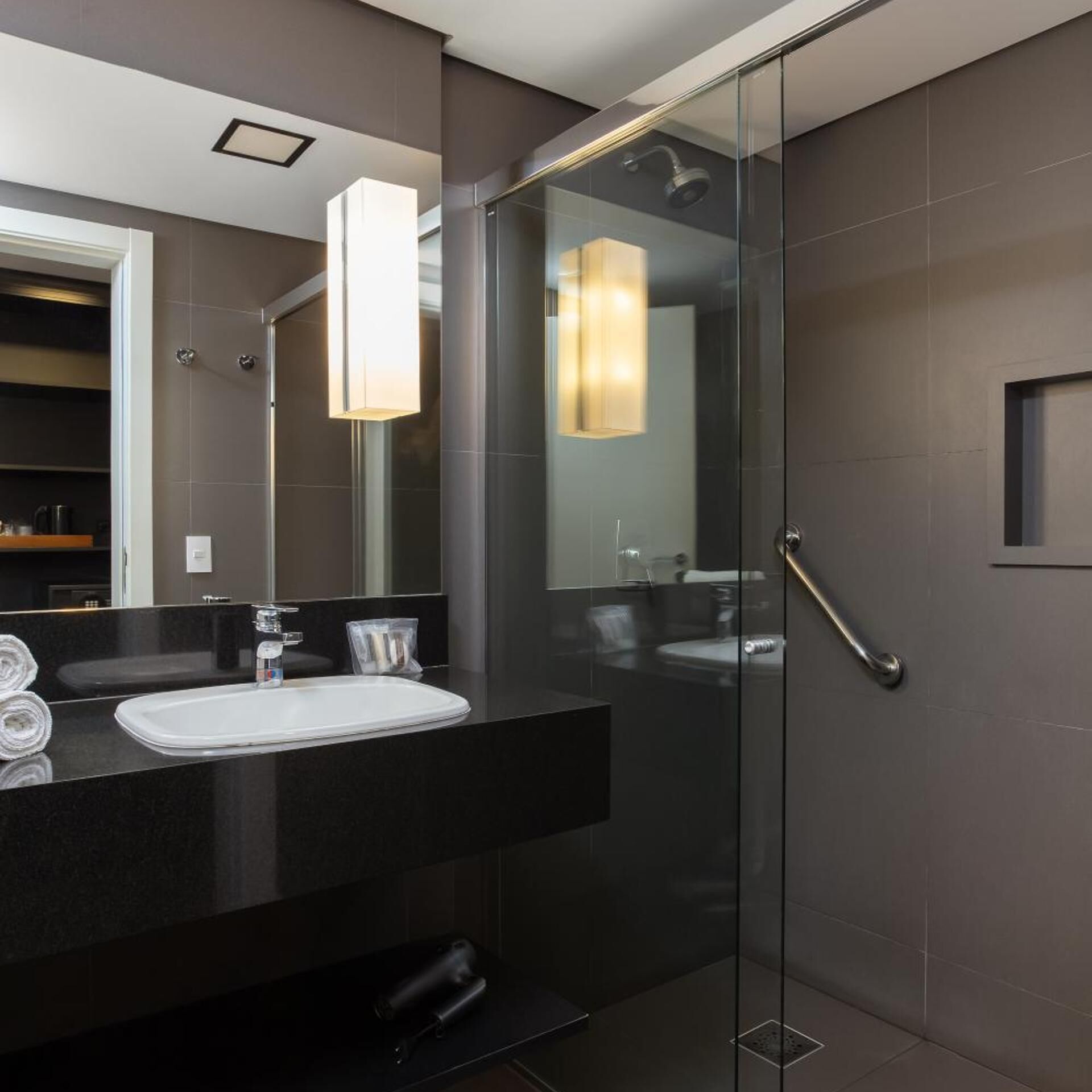 A modern bathroom with a glass shower enclosure, a black countertop, and a large mirror.