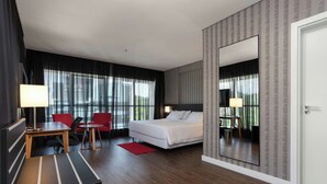 A hotel room with a bed, a desk, a chair, a red rug, and a large mirror. - Hilton Garden Inn Itajai (Itajai)