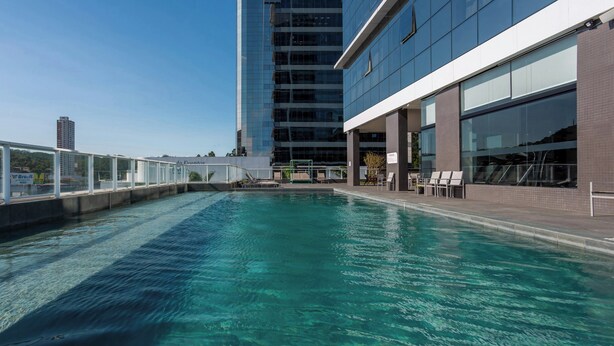 A rooftop pool with clear water, surrounded by a modern building with large windows and a glass facade. - Hilton Garden Inn Itajai (Itajai)