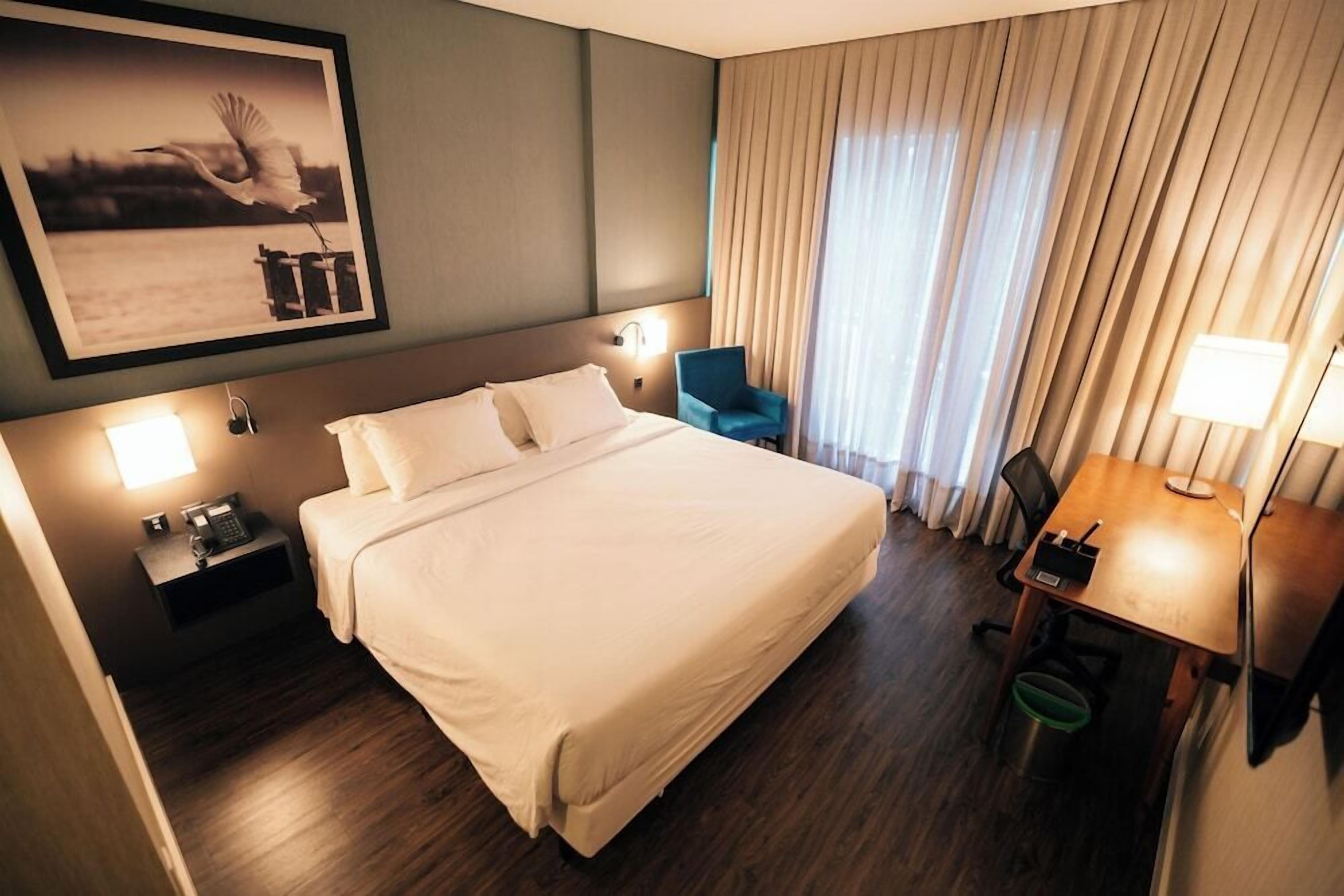 A hotel room with a large bed, bedside lamps, a desk with a chair, and a framed picture on the wall.
