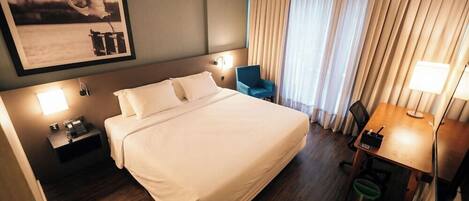 A hotel room with a large bed, bedside lamps, a desk with a chair, and a framed picture on the wall.