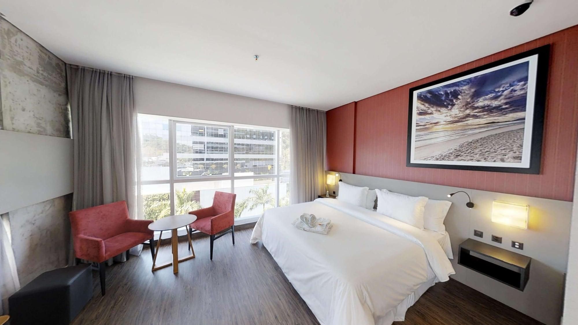 Una camera d'albergo con un letto grande, una scrivania, due sedie, una finestra vista edifici e un quadro appeso al muro.