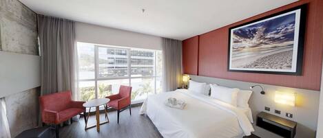 Una camera d'albergo con un letto grande, una scrivania, due sedie, una finestra vista edifici e un quadro appeso al muro.
