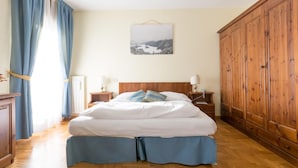 A bedroom with a wooden bed, a nightstand, a dresser, and a large wardrobe. - Hotel Belvedere (Pieve di Cadore)