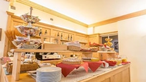 A buffet setup with various food items and beverages, a wooden counter, and a hanging decorative item. - Hotel Belvedere (Pieve di Cadore)