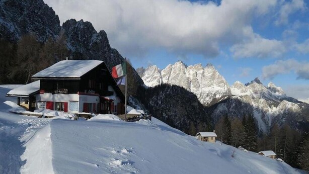 A snow-covered mountain lodge with a red and white facade, surrounded by snow-covered peaks and a clear sky. - Hotel Belvedere (Pieve di Cadore)