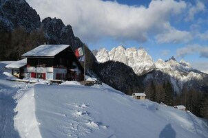 Ein schneebedecktes Berghotel mit roter und weißer Fassade, umgeben von verschneiten Berggipfeln und einem klaren Himmel.