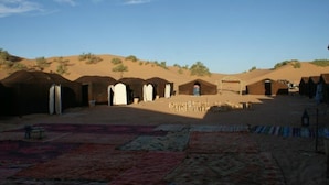 A desert landscape with traditional tents and a carpeted area. - Tizi Plus Desert (Zagora)