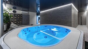 A modern indoor swimming pool with a textured edge, surrounded by a minimalist design with a clock and shelves on the walls. - Grand Baltic Dunes (Palanga)