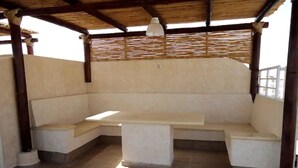 Un espace extérieur abrité, aménagé avec un banc et une table, soutenu par des poutres et des colonnes en bois.