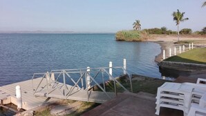 Une zone côtière avec une jetée en bois menant à l’eau, des chaises longues blanches et une vue dégagée sur la mer.