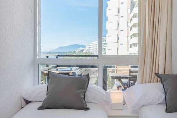 A hotel room with a large window offering a view of a cityscape and mountains.