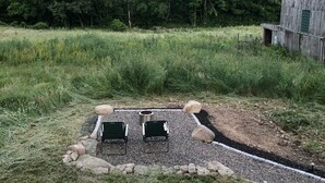 A rustic outdoor seating area with two chairs and a fire pit, surrounded by a gravel path and a wooden fence. - Relax and unwind at Solar Solitude (Mathias)