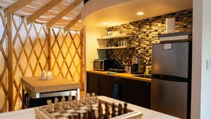 A compact kitchen with a microwave, refrigerator, and wooden table with chess pieces. - Relax and unwind at Solar Solitude (Mathias)