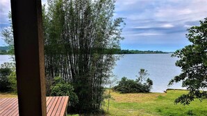 A view of a lake from a wooden deck with a grassy area and trees in the foreground. - Cabana à Beira D'água Linda Vista (Imbituba)
