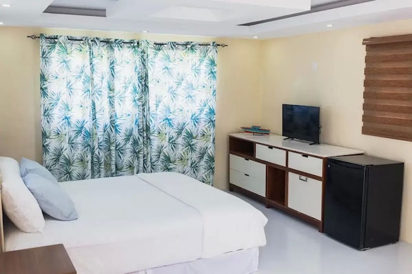 Un dormitorio con una cama, un televisor, un mueble negro pequeño y un mueble de madera con cajones.