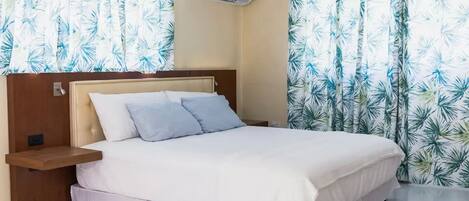 A neatly made bed with a wooden headboard, a bedside table, and a wall-mounted air conditioner.