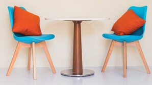 Deux chaises bleues avec des coussins orange et une table ronde dotée d’un pied métallique.