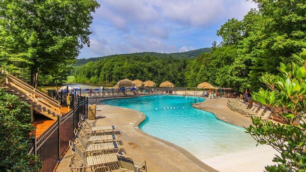 A swimming pool with a curved design, surrounded by lounge chairs and umbrellas, set against a backdrop of lush greenery and hills. - Petit Crest Villas (Jasper)