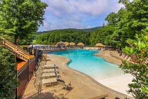 A swimming pool with a curved design, surrounded by lounge chairs and umbrellas, set against a backdrop of lush greenery and hills. - Petit Crest Villas (Jasper)