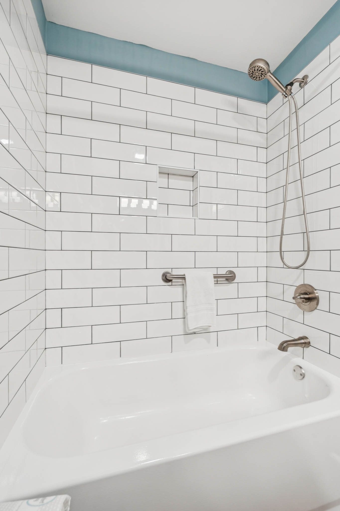 A bathroom with white tiled walls, a white bathtub, and a showerhead.