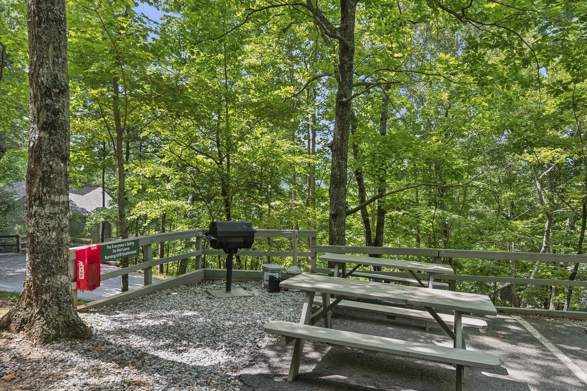 Un espace pique-nique équipé de bancs et d’un barbecue, entouré d’arbres.