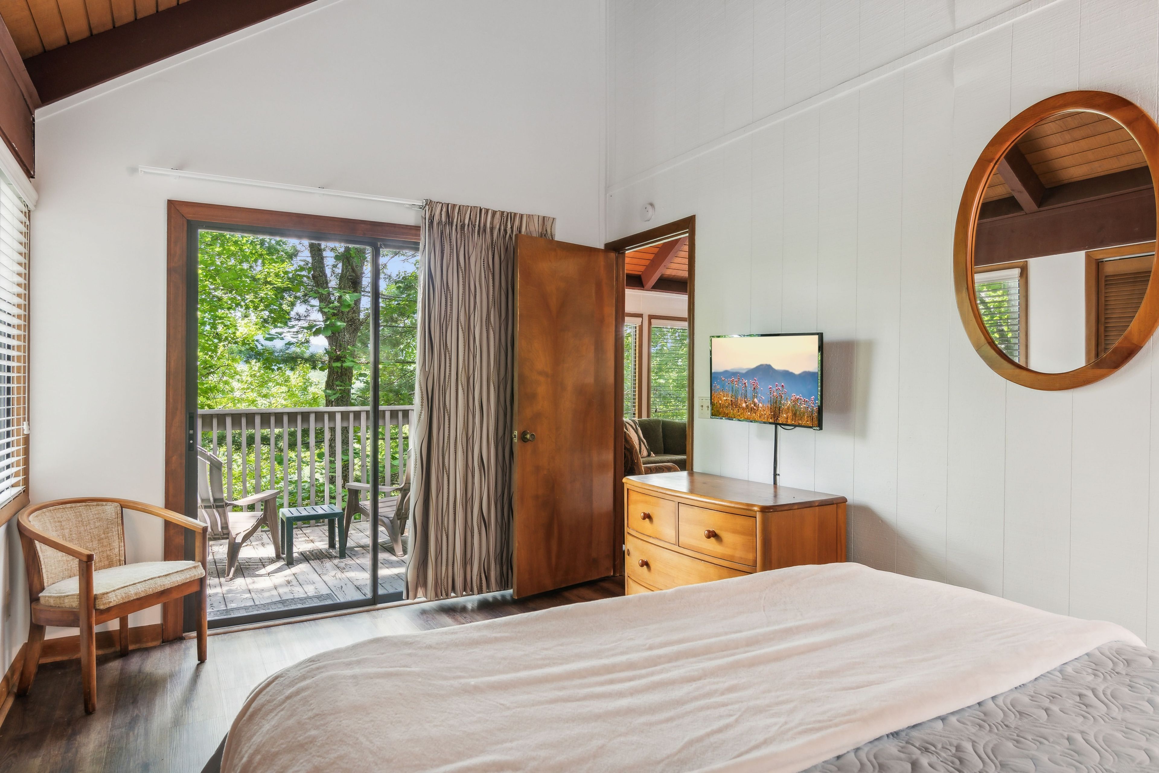 A bedroom with a large bed, a dresser, a chair, a television, and a sliding glass door leading to an outdoor area.