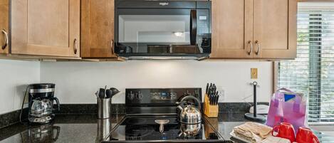 Una cocina con armarios de madera, un microondas, una estufa y una cafetera.