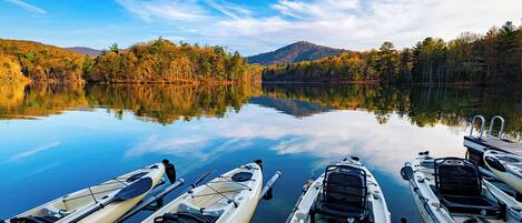 Un lago tranquilo con kayaks amarrados en la orilla, rodeado de árboles y montañas.