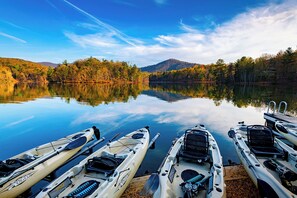 A calm lake with kayaks docked on the shore, surrounded by trees and mountains. - Petit Crest Villas (Jasper)