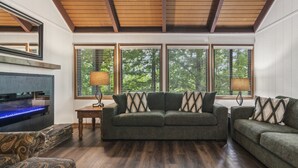 A cozy living room with a green sofa, a fireplace, and large windows with blinds. - Petit Crest Villas (Jasper)