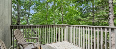 A wooden deck with two Adirondack chairs, surrounded by a white railing, overlooking a forested area.
