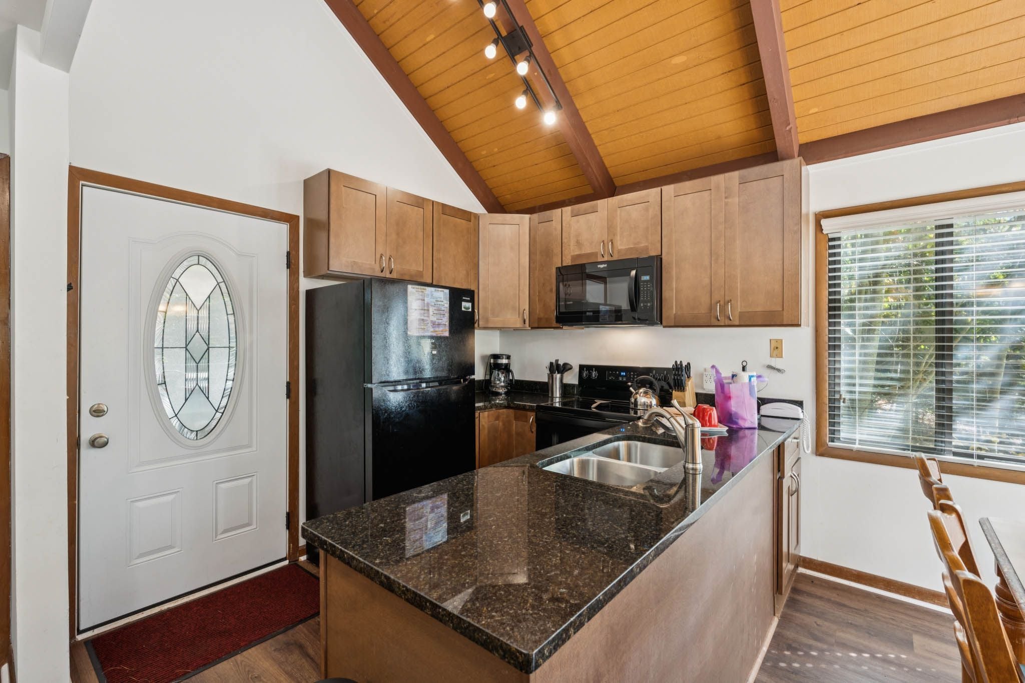 A kitchen with wooden cabinets, a black refrigerator, a microwave, a coffee maker, and a granite countertop.