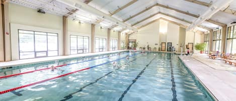 Ein großer, überdachter Schwimmbereich mit deutlichen Bahnen, hoher Decke und großen Fenstern.